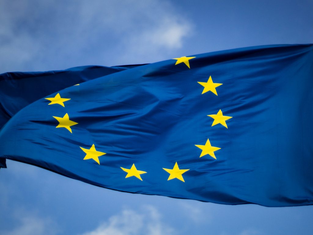 EU-lipussa on tähtiä ympyrämuotoon. Taustalla on sininen taivas ja kevyitä oilviä.